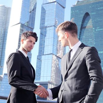 Business people shaking hands on skyscraper background