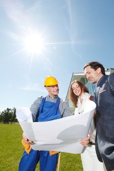 Worker shows house design plans to a young couple at construction site