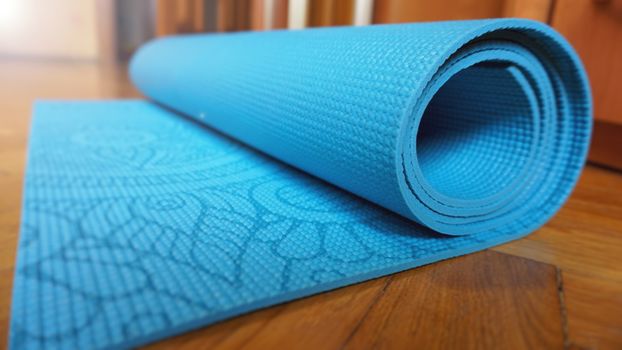 Close up of yoga, fitness floor mat at home in a roll. Yoga props and accessories, aqua turquoise mat. Healthy lifestyle concept