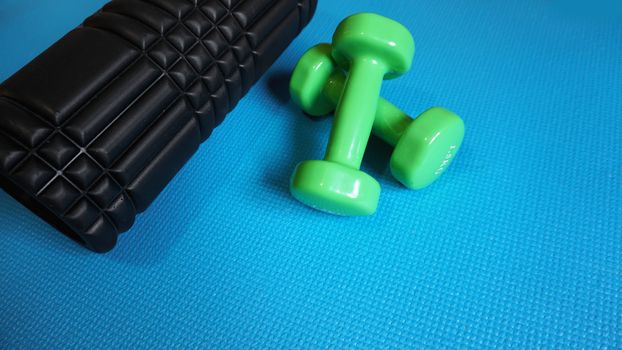 Foam Roller with green dumbbells Gym Fitness Equipment Blue background self Myofascial Release - MFR.