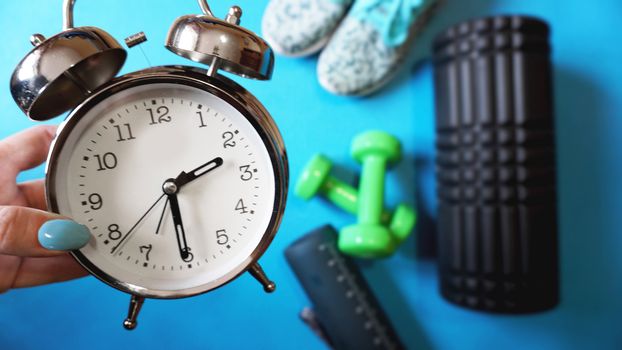 Blue yoga mat, two dumbbells, alarm clock, self-massage roll, sneakers and water bottle - time for sport