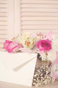 Basket of flowers and blank envelope on wooden background