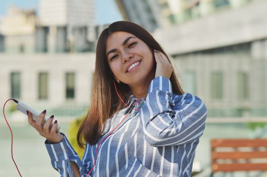 Beautiful portrait of a brunette girl of Asian appearance who listens to music walking around the city