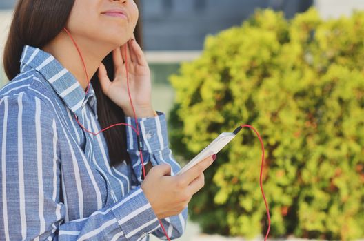 Young girl student holding a phone and listening to music on the street in the Park