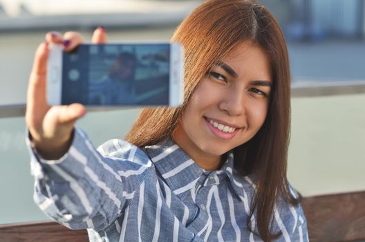 Portrait of a brunette girl walking around the city who makes a selfie with an outstretched hand on the street