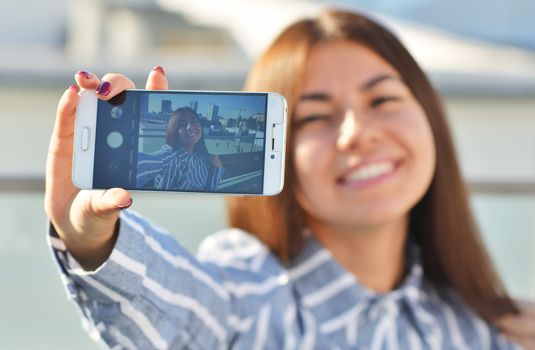 A girl student of Asian appearance smiles beautifully and makes a selfie while on the street