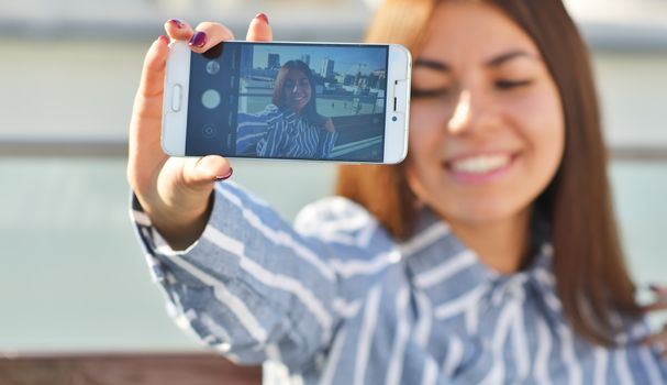 Attractive girl student smiles with her eyes closed and takes a selfie at arm's length