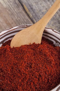 Red paprika in a ceramic bowl with brown wood spoon on old wood table 