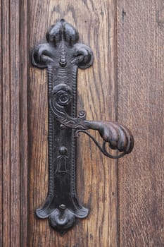 Ancient rusty church door handle on brown old wooden door