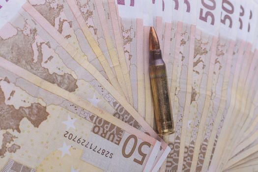 Single rifle bullet closeup with a pile of euro banknotes in the background