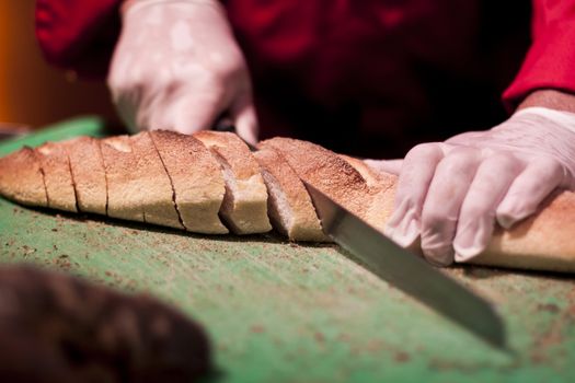 Slicing fresh baked bread with long knife moving hands 