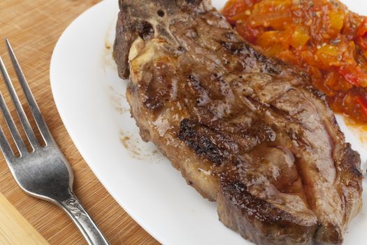 Grilled  steak with vegetable garnish and some black peppers on white plate and wood background