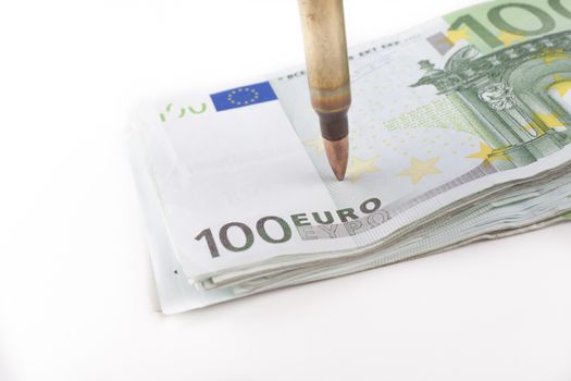 Single rifle bullet closeup pointing at  a pile of a hundred euro banknotes in the background isolated on white