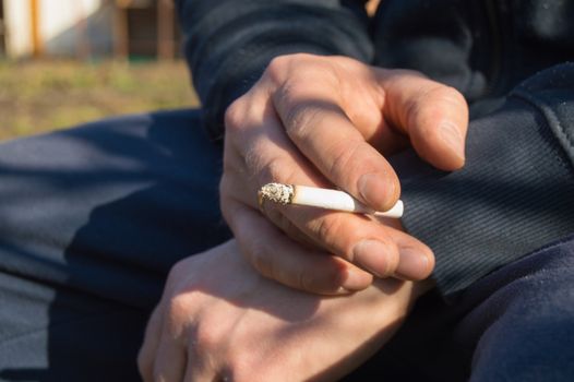 A young man holding a cigarette in his hand, sitting outdoors.