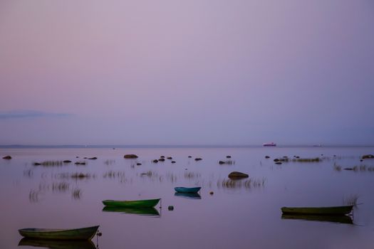 Fishing boats are anchored in a row, reflected in a clear lake at dusk.