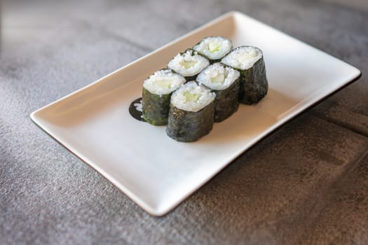 Cucumber Sushi served  on rectangular white plate on dark gray stone background