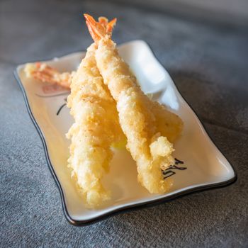 Tempura shrimps served  on rectangular white plate on dark gray stone background