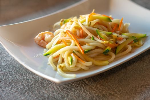 Yaki udon served  on rectangular white plate on dark gray stone background