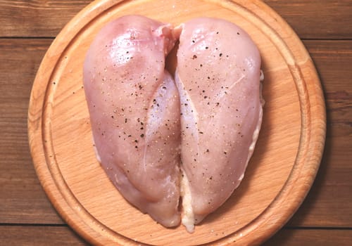 Two raw chicken fillets lie on a wooden Board on a wood background. Meat is located in the center