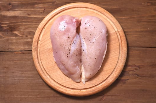 Two raw chicken fillets lie on a wooden Board against a wood background. Meat is located in the center