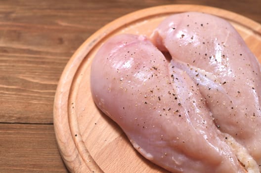 Heart of raw chicken breast close up on wooden Board. Meat sprinkled with salt and pepper