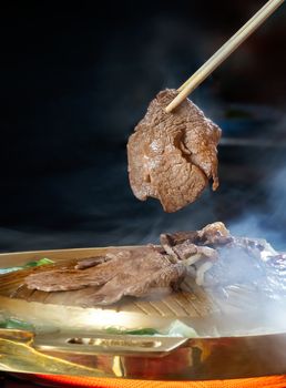 a piece of grilled beef pinched by chopsticks , Asian style hot pan