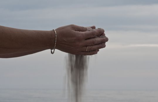 sand falls from the hand of a woman as an image of time passes