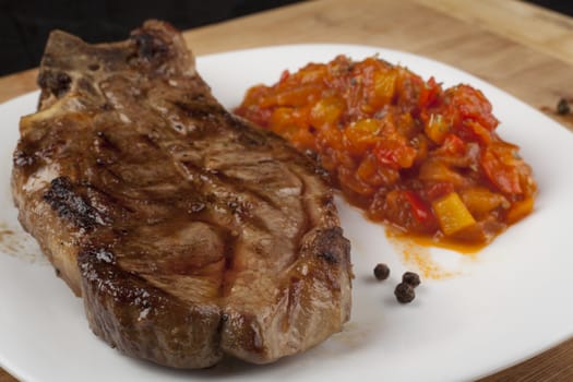 Grilled  steak with vegetable garnish and some black peppers on white plate