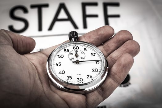 Dramatic locking hand holding silver color analog stopwatch with staff t-shirt in the background