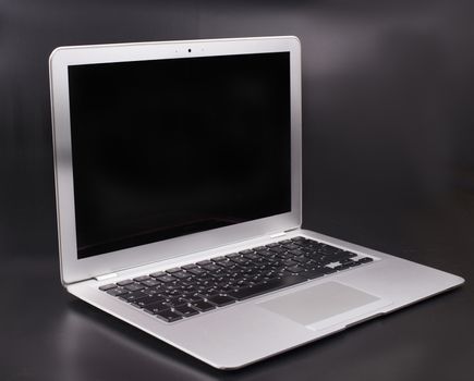 Slim silver color laptop on a dark background with black blank screen