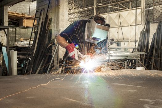 Welder working in a steel factory with sparks flying on working table