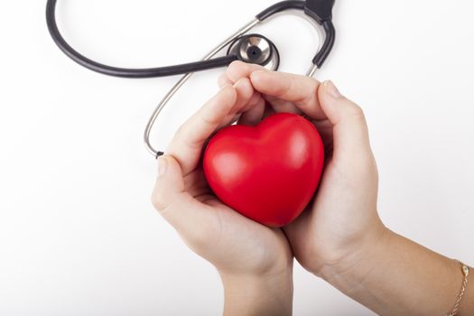 Holding red heart in two hands with black stethoscope in the background isolated on white