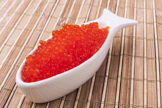 Red caviar in a fish shape white bowl on brown wooden background