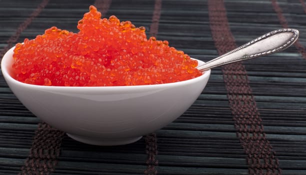 Red caviar in a white bowl on black wooden background with silver spoon