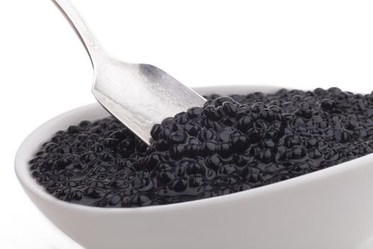 Black caviar beads in white bowl and silver spoon close-up isolated on white background