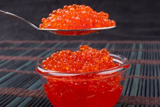 Red caviar on a spoon close-up on dark background