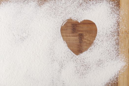 Heart shape flour on brown wood cutting board