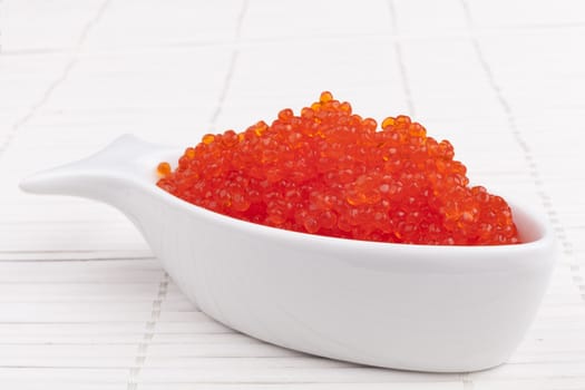 Red caviar in a fish shape bowl on white wooden background
