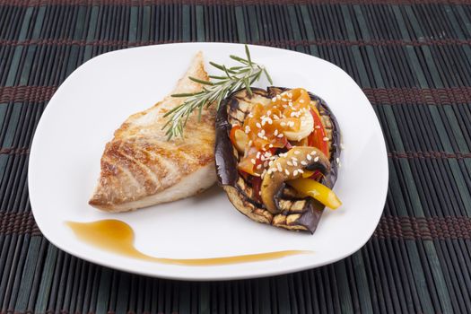 Fish and vegetables on eggplant in white plate on dark background