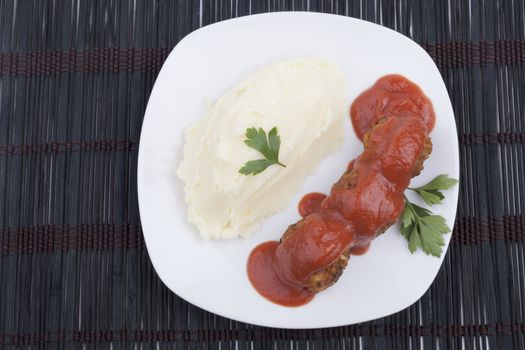 Meatballs with red tomato sauce adn mushed potato on white plate on dark background
