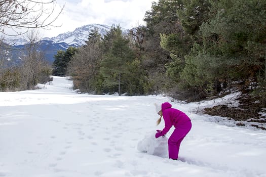 Young woman make a snowman on a sunny day in the winter snow-covered forest in the mountains.