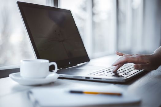 Woman in office using laptop and notepad to work. Shallow depth of field.