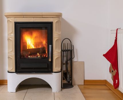 Tiled stove with fire burning inside, cosy and warm interior scene, heating in winter, Christmas decoration on the wall
