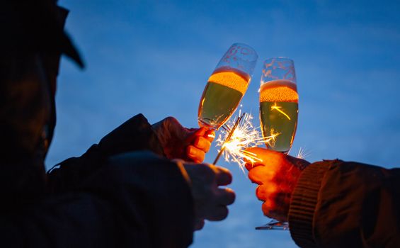 hands of elderly couple holding sparkles and glasses of champagne celebrating New Year