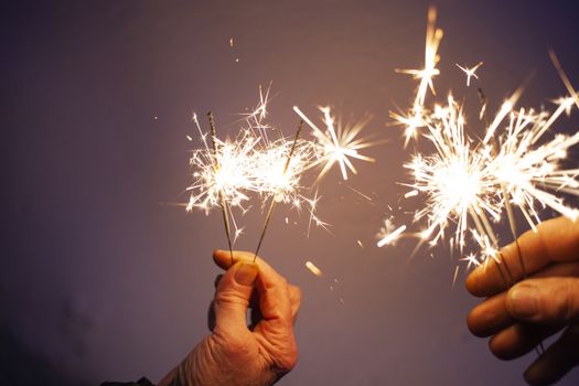 hands of elderly couple holding sparkles celebrating New Year