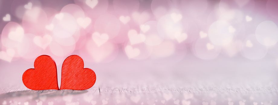 Two small handmade red wooden hearts on bright pink lights bokeh background