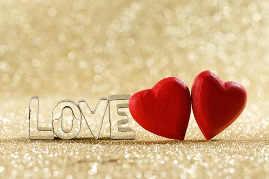 Two red handmade wooden hearts and word love on golden bright glitter lights bokeh background