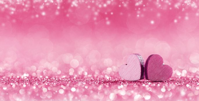 Two small handmade pink wooden hearts on bright lights bokeh background