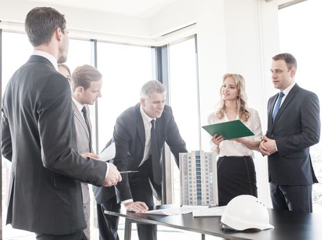 Business meeting of architects and investors looking at model of modern multi storey residential building house on table