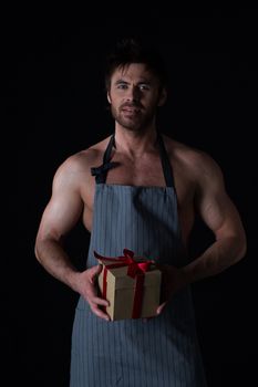 Handsome muscular naked man in an apron holding holiday gift box